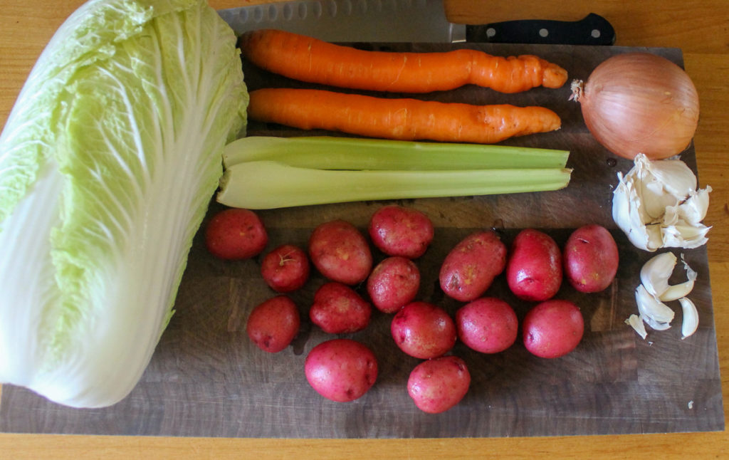 Beef Cabbage Soup Ingredients on a cutting board including baby red potatoes, celery, carrots and a head of cabbage.