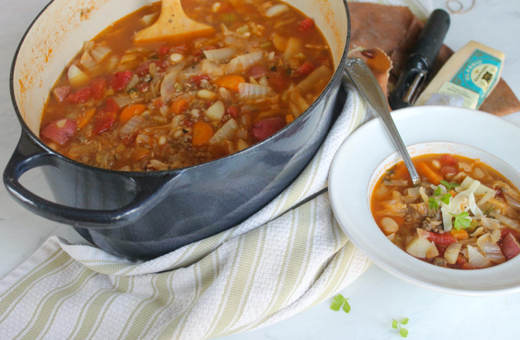 Pot of Beef Cabbage Soup next to a white bowl of soup.