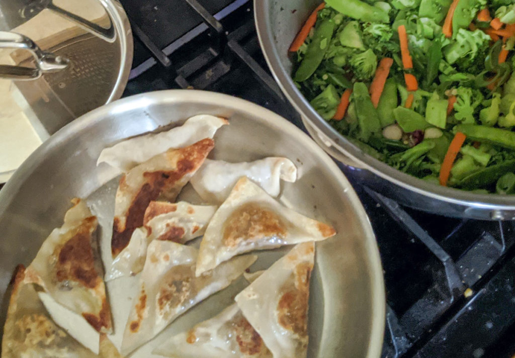 Pan of potstickers cooking, and stir frying vegetables.