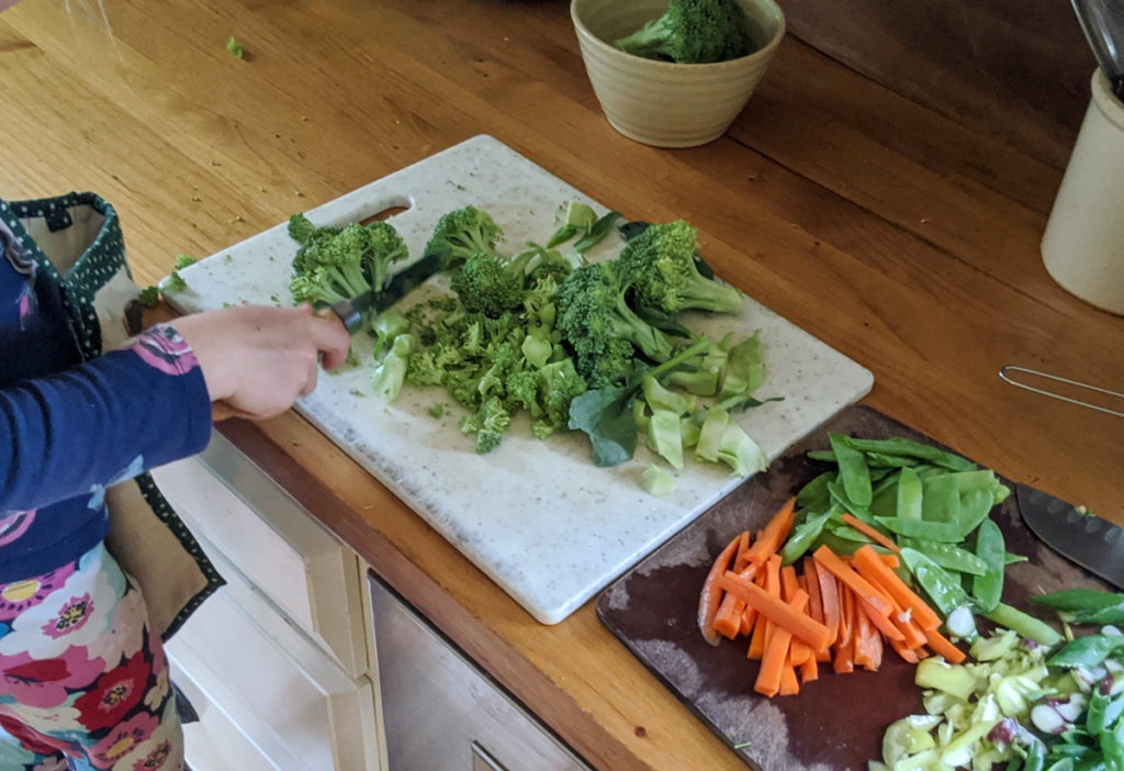 Child chopping broccoli and other veggie for stir fry.