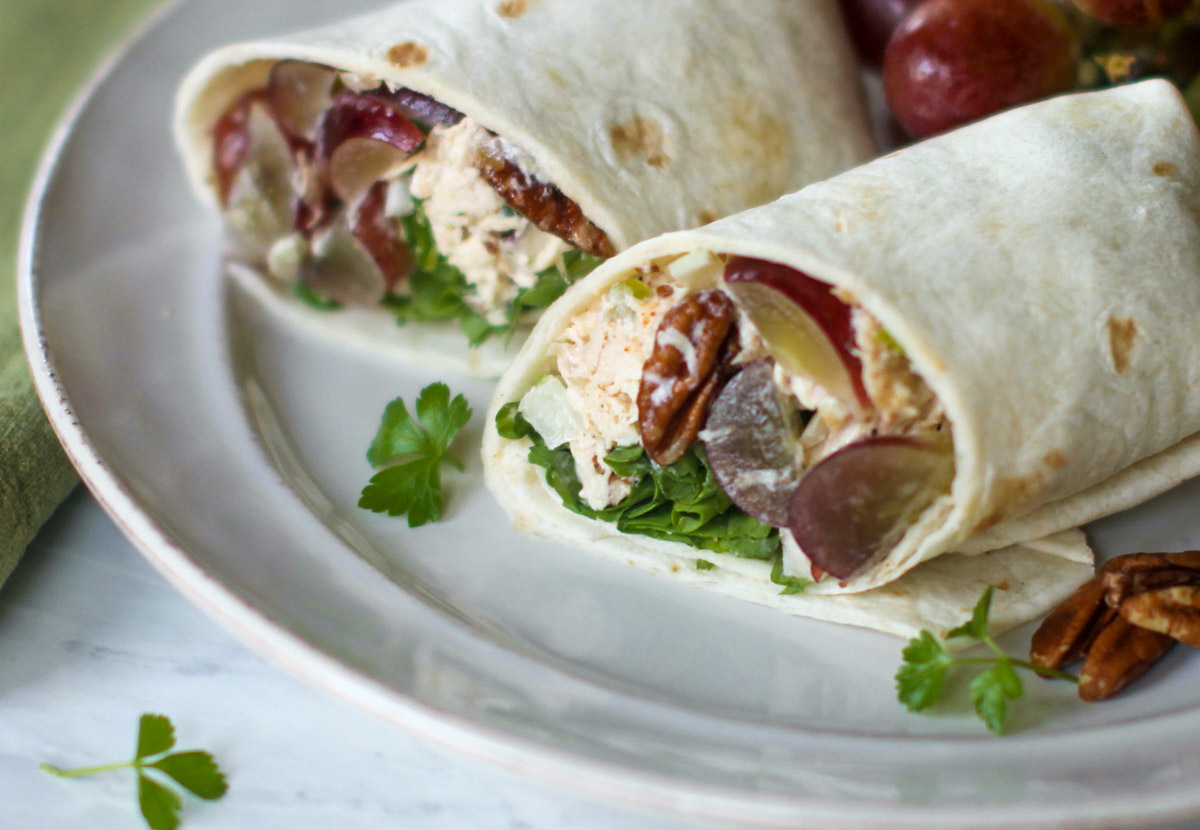 A Chicken Salad Wrap sliced in half on a plate with grapes.
