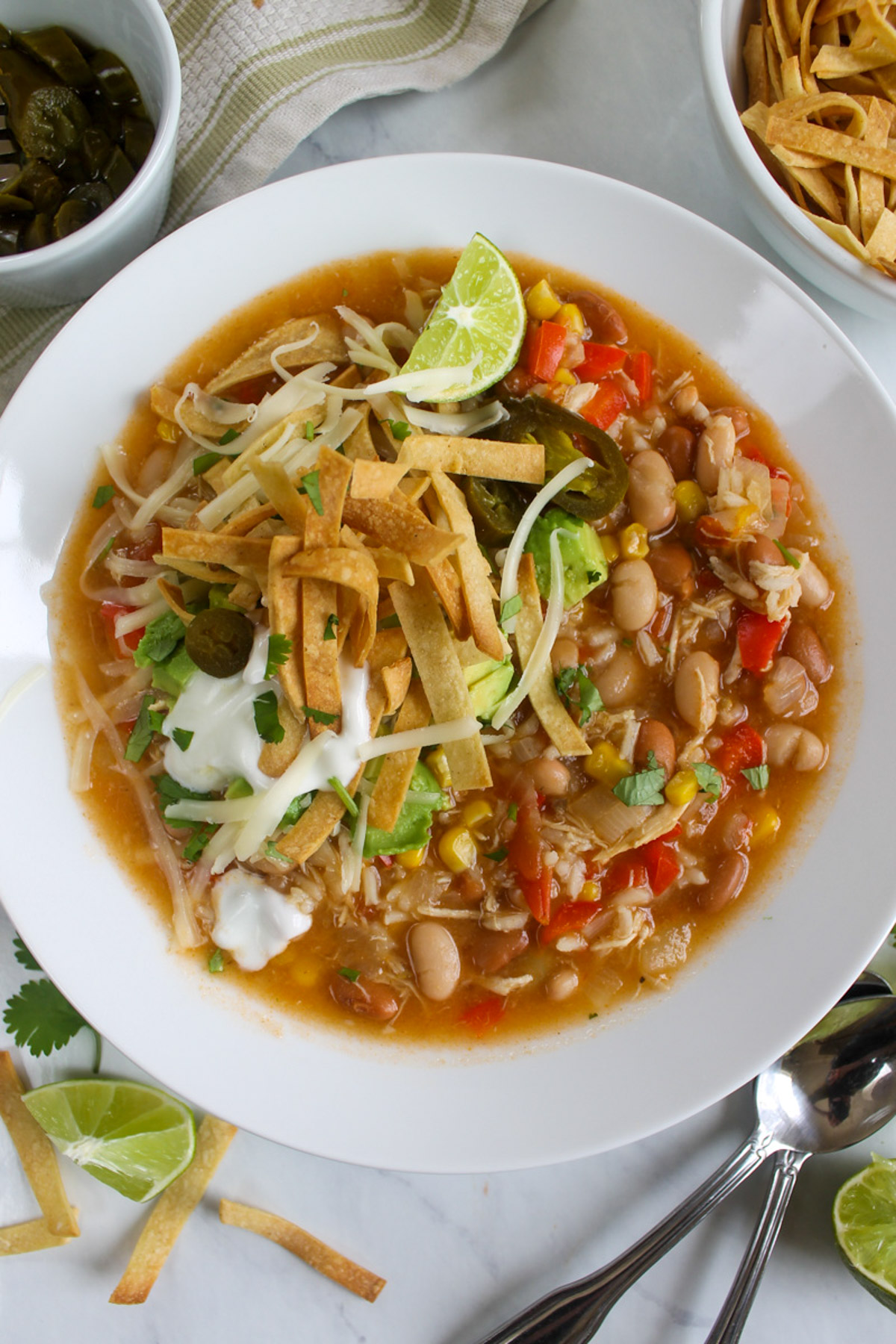 A top down look at a bowl of chicken tortilla soup with lots of toppings, crispy tortilla strips and lime wedges.