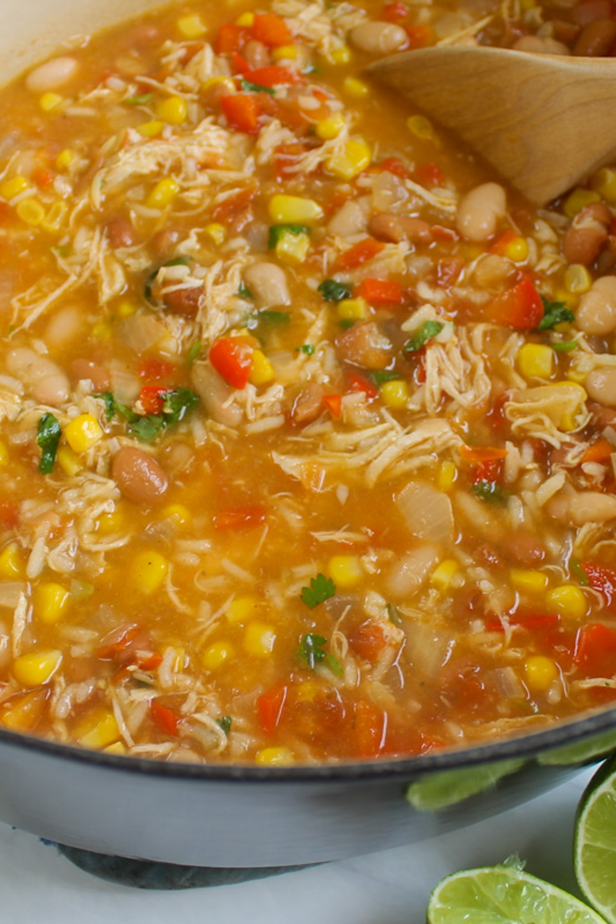 A soup pot full of chicken tortilla soup in a red tomato broth with shredded chicken, beans, and corn.