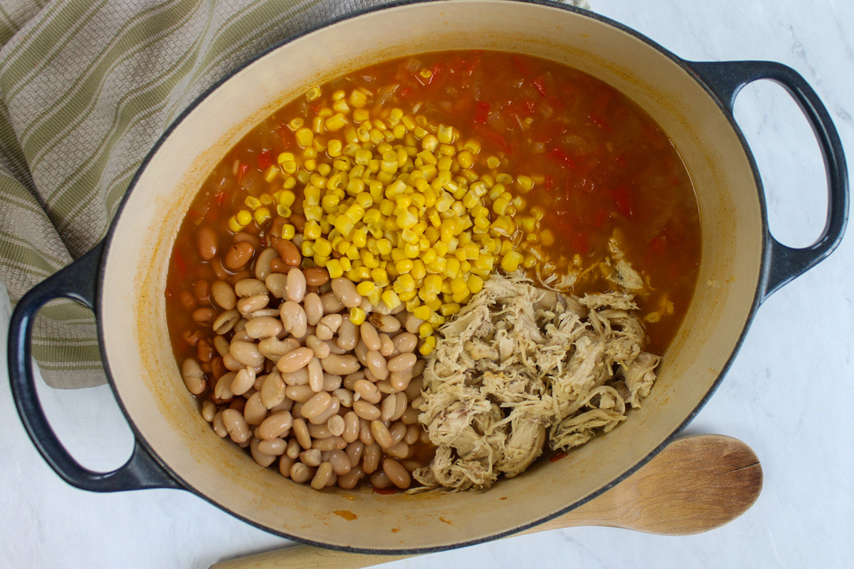 Adding beans, corn and chicken to the simmering soup.
