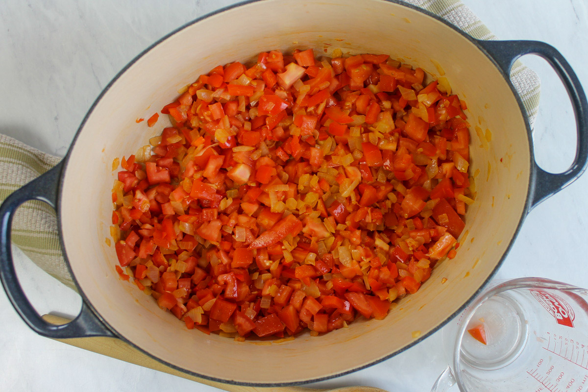 Onions, red bell pepper and tomato cooking in a soup pot and seasoned with spices for chicken tortilla soup.