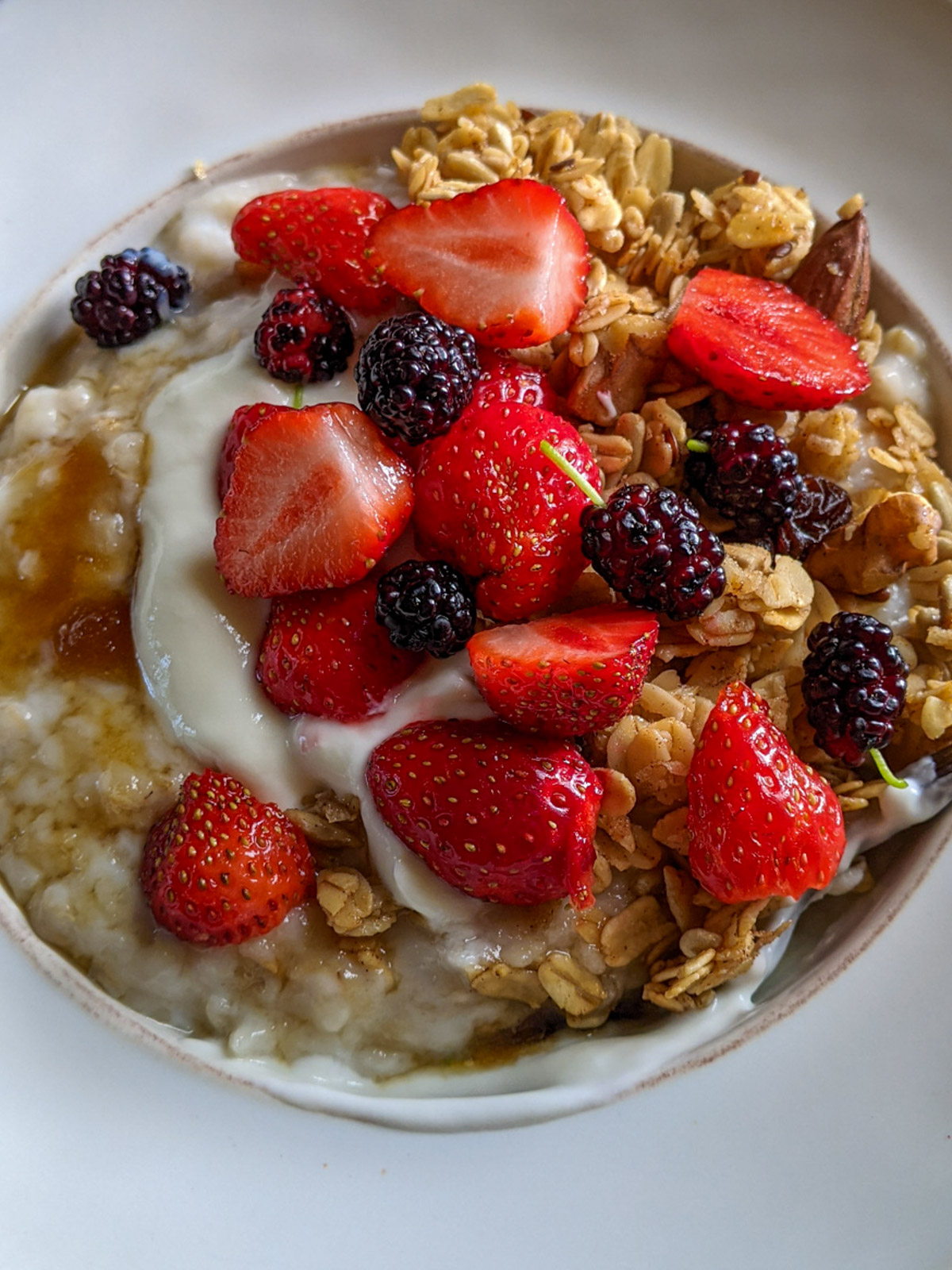 A bowl if Crockpot Steel Cut Oatmeal topped with strawberries, mulberries, yogurt and granola.