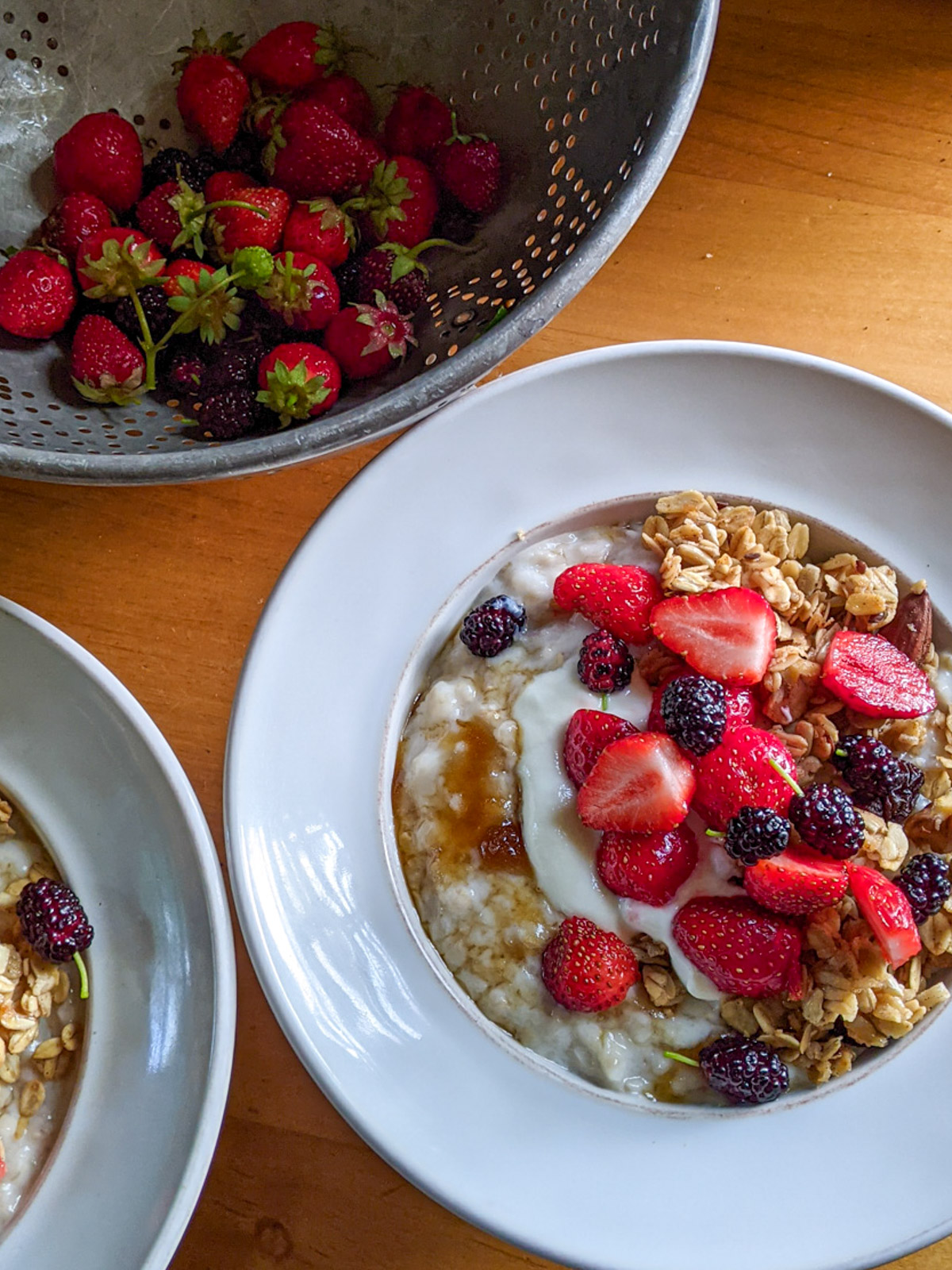 A bowl of slow cooker steel cut oatmeal with toppings next to a strainer full of fresh strawberries.