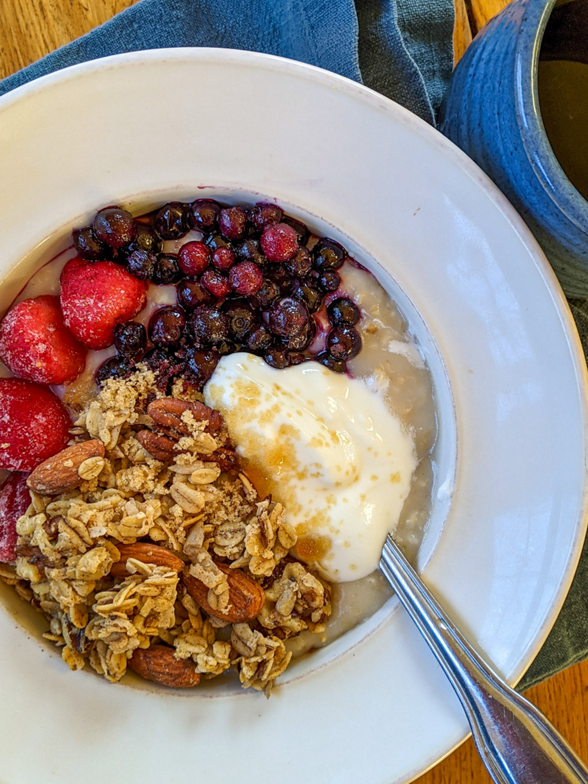 A white bowl of Crockpot Steel Cut Oatmeal with frozen blueberries and strawberries, yogurt, brown sugar and granola. 