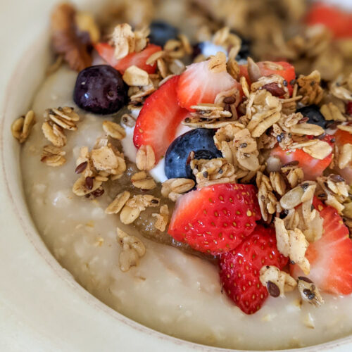A close up of creamy steel cut oats with berries and granola.
