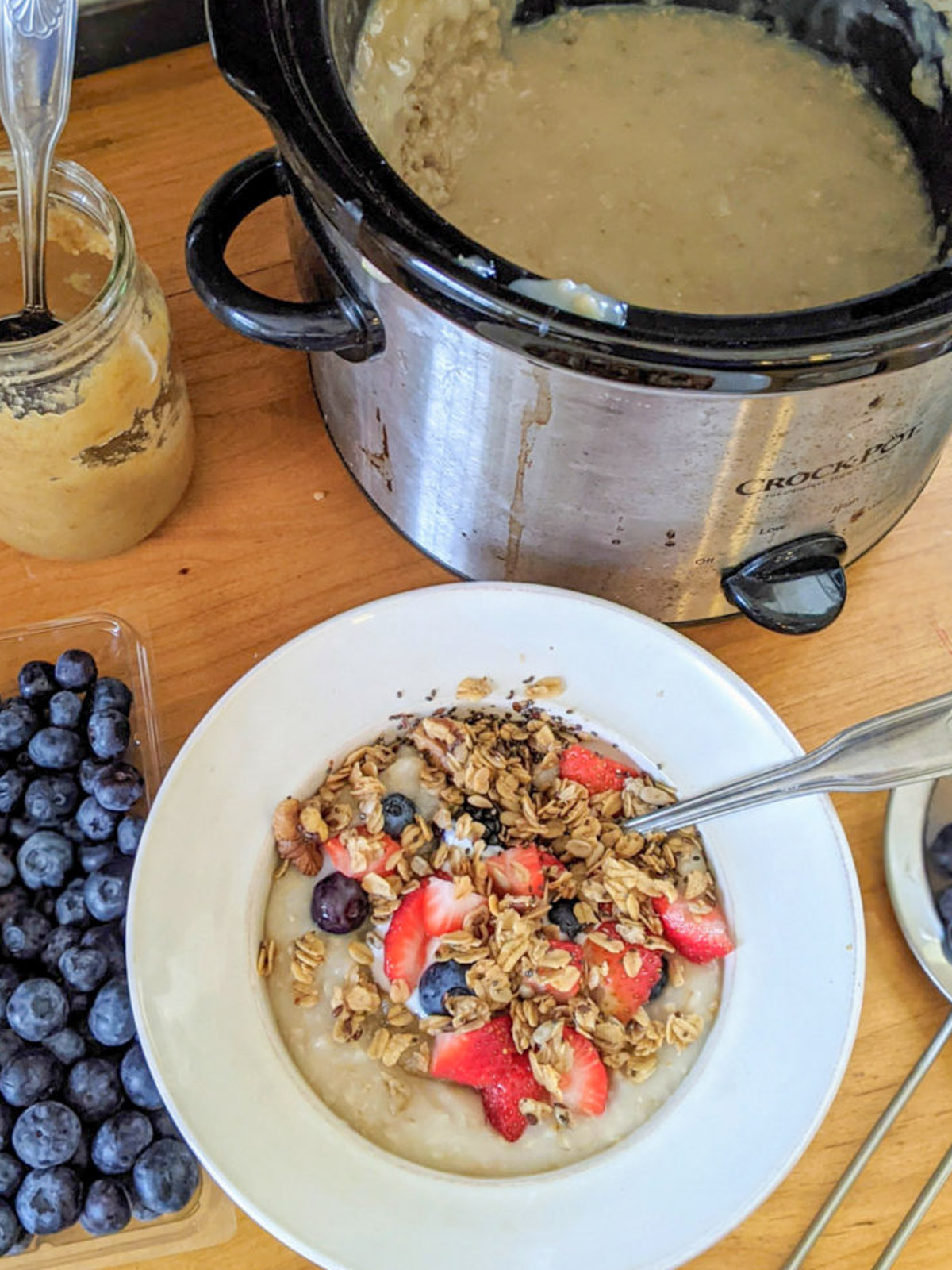 A crockpot full of overnight steel cut oatmeal with a bowl of oatmeal with berries and granola.