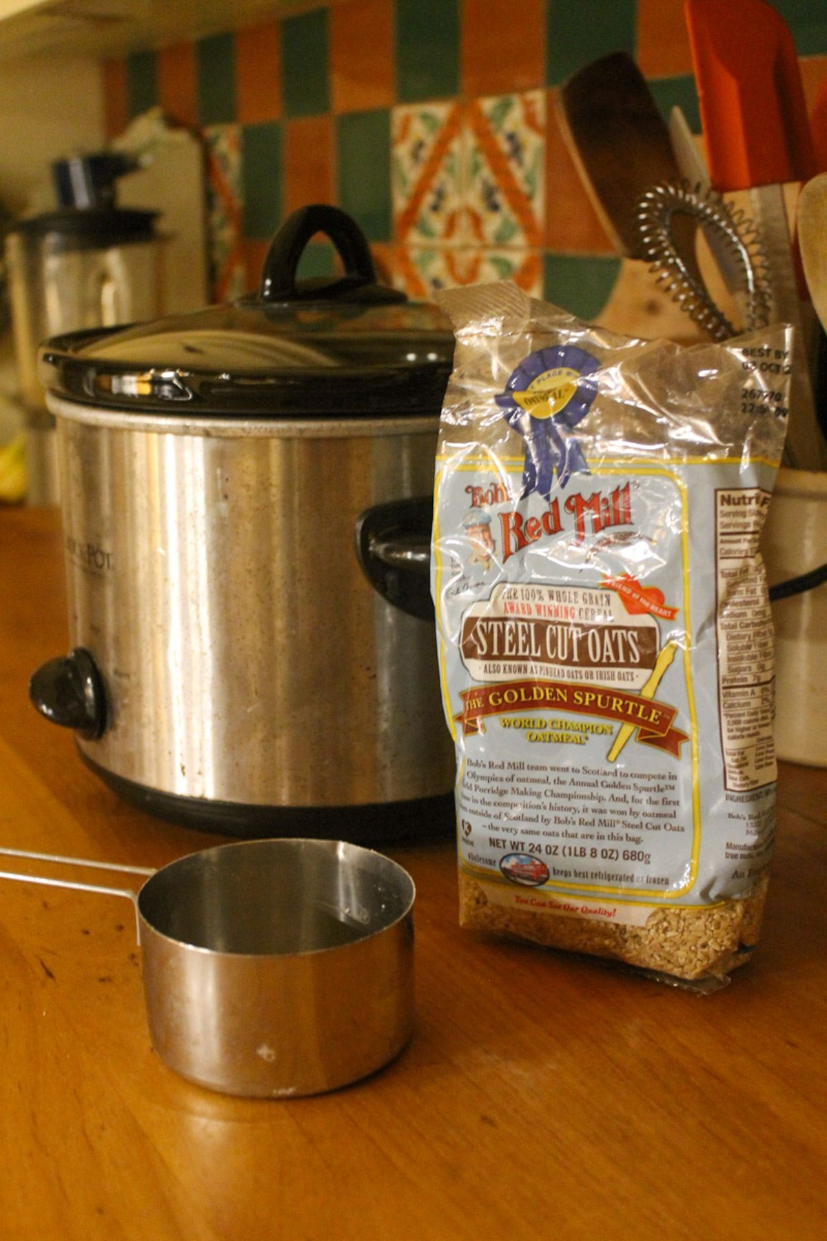 A crockpot on the counter next to a bag of steel cut oats and a measuring cup, ready to cook overnight. 