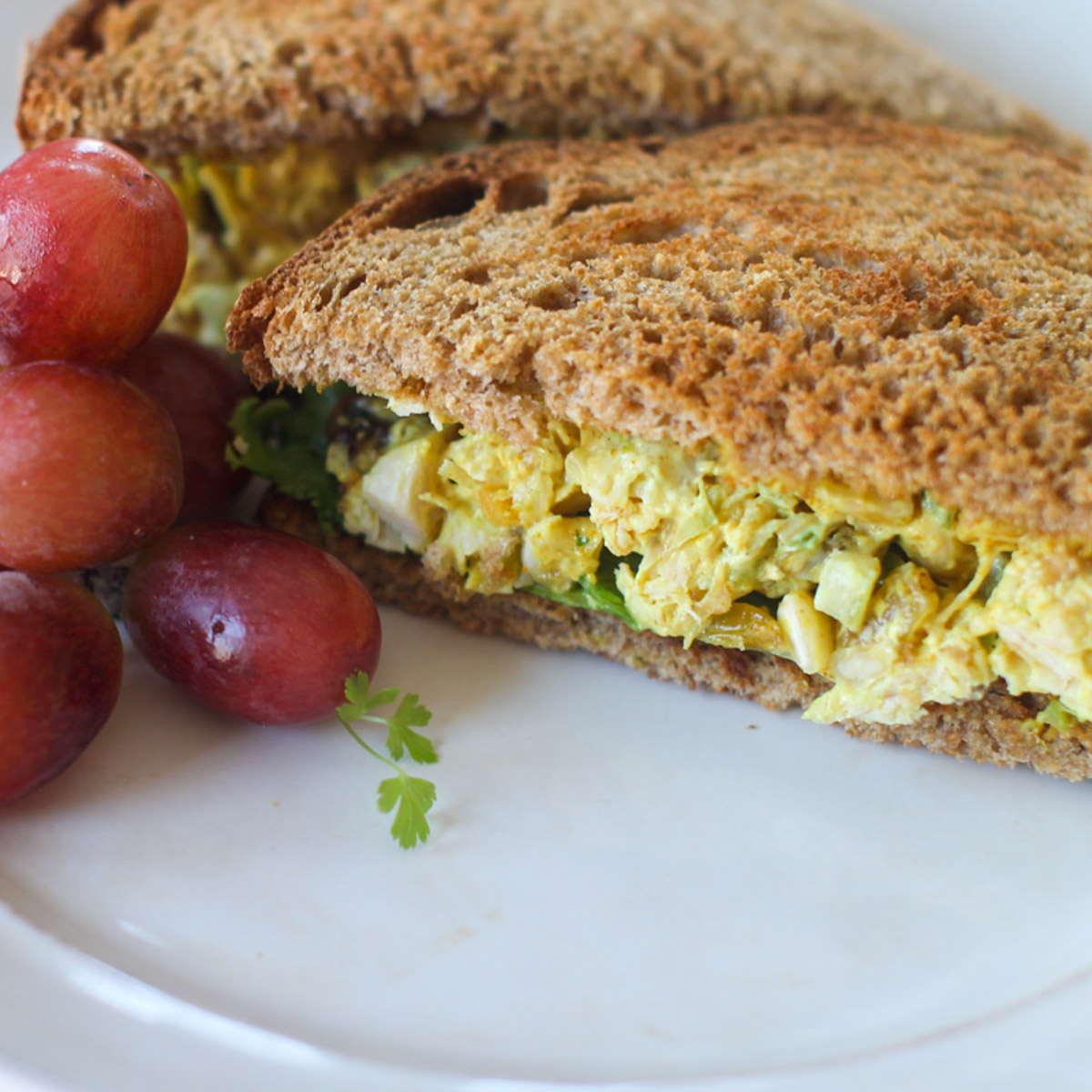 Curry Chicken Salad Sandwich on wheat bread next to red grapes.