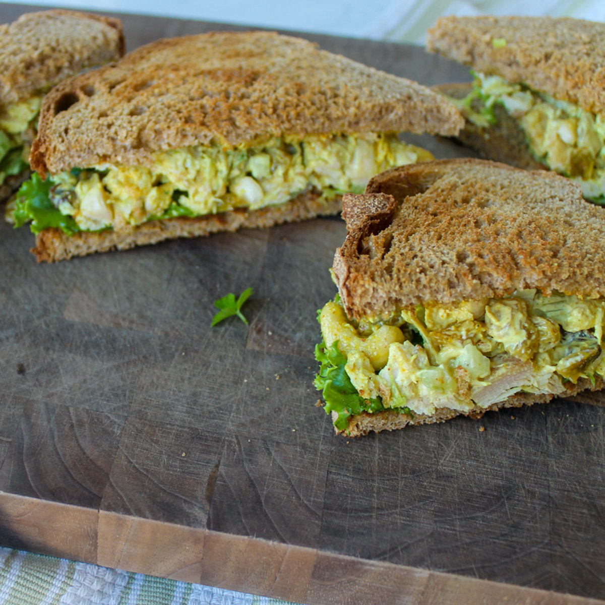Curry Chicken Salad Sandwiches on wheat bread with lettuce, sliced on a cutting board.