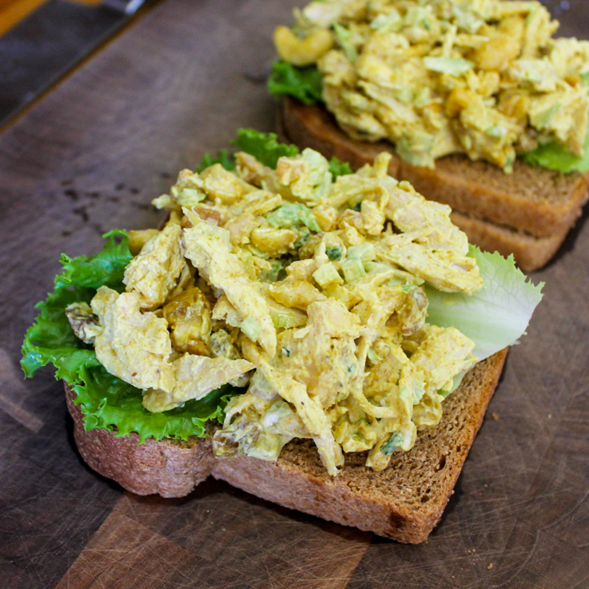 Curry Chicken Salad being prepared on toasted sandwich bread with lettuce.