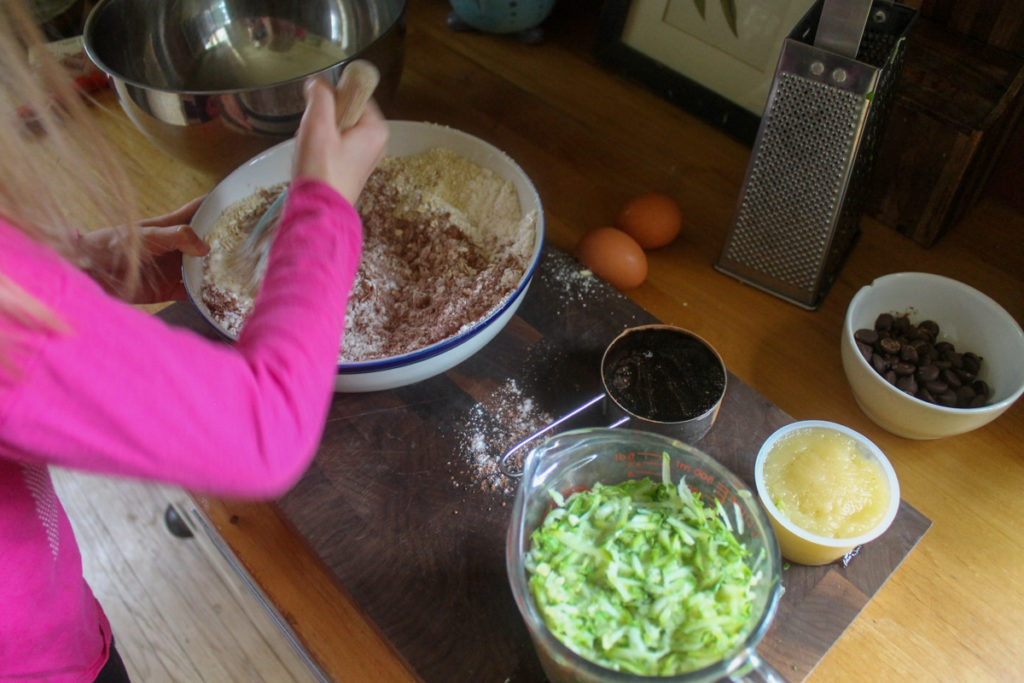 Child mixing dry ingredients for chocolate zucchini batter.