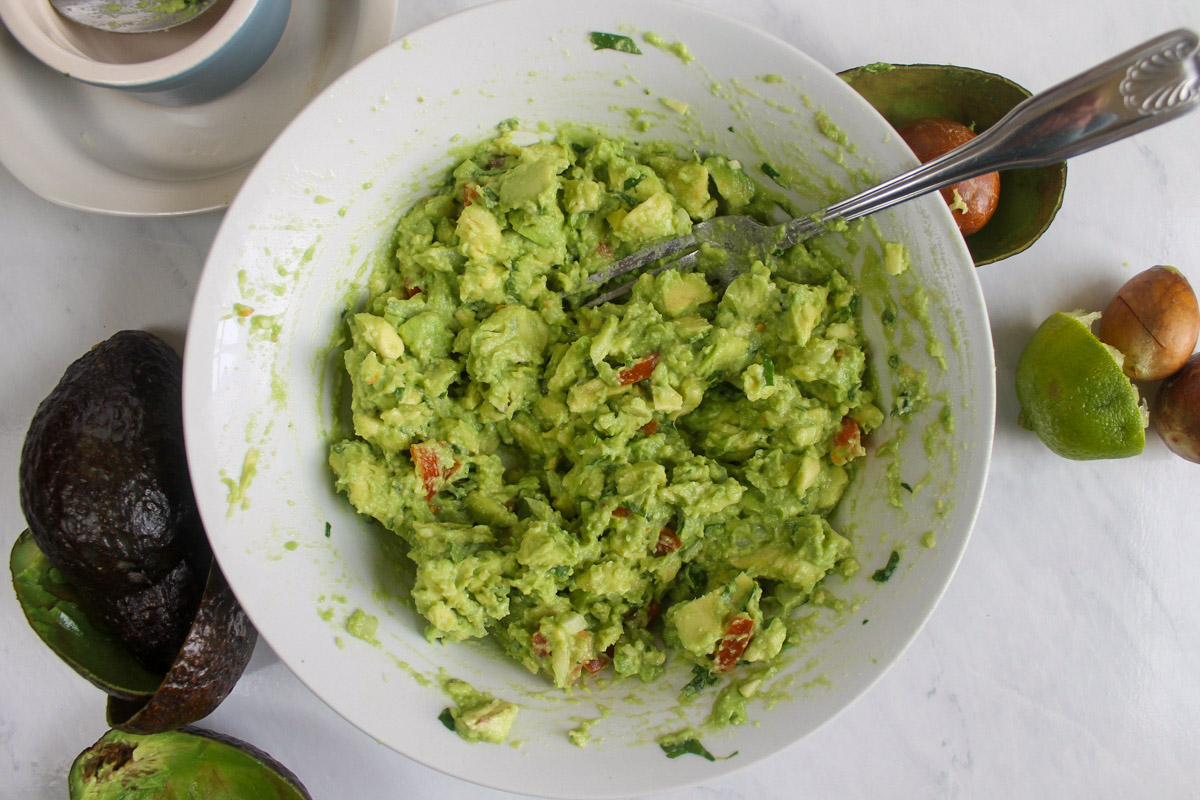 Mashing avocados with all guacamole ingredients in a bowl.