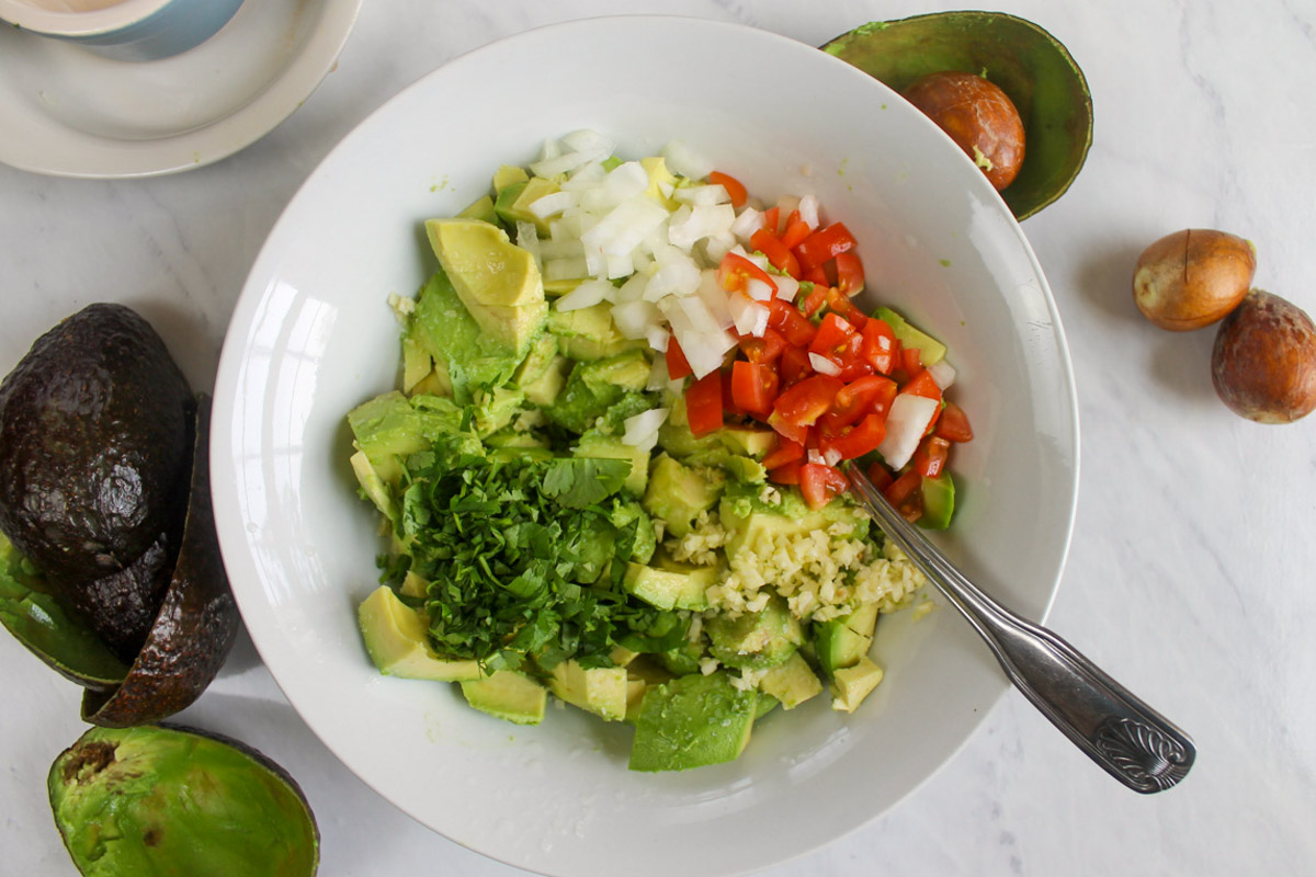 Ingredients for guacamole added to a bowl ready to mix.