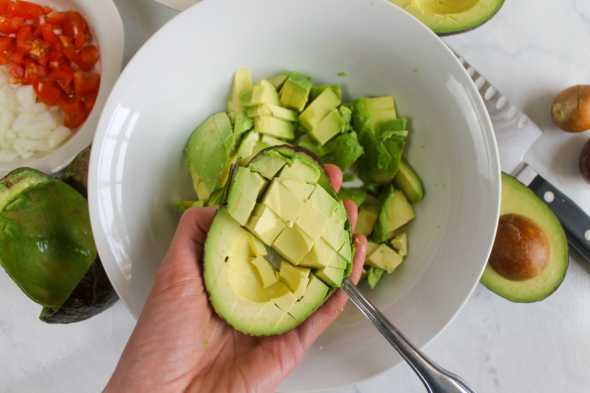 Peel and chopping avocados for guacamole into a white bowl.