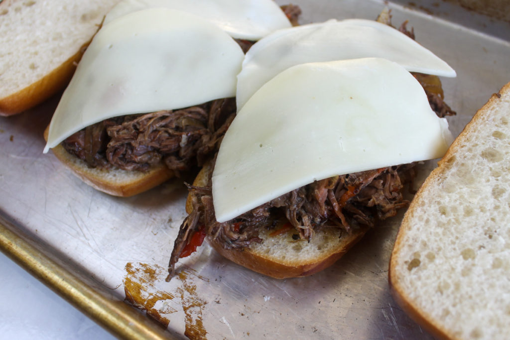 Assembling Hoagies with shredded Italian beef and provolone cheese ready to be toasted.