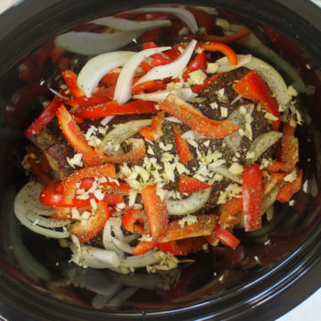 Italian beef roast being prepared in the slow cooker with onions, peppers and garlic.