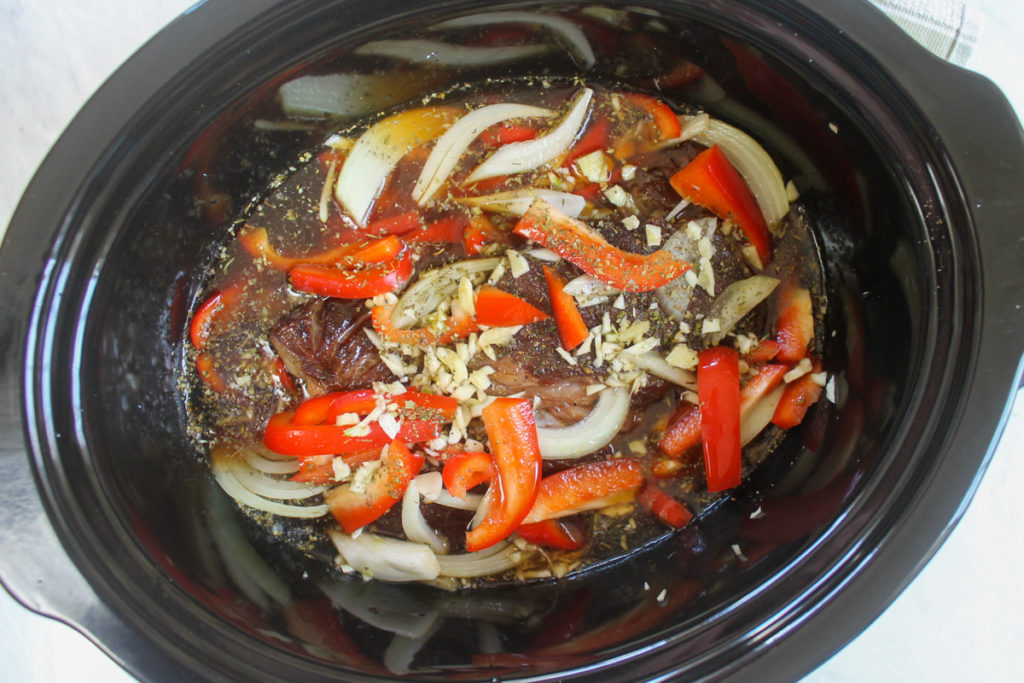 Italian beef in the crock pot with veggies and beef stock ready to cook.