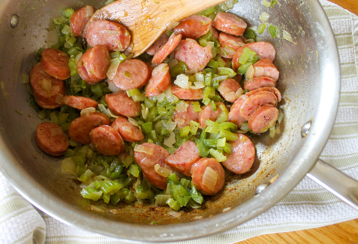 Sauteed sausage and vegetables in a skillet, ready to add rice, tomato and stock.