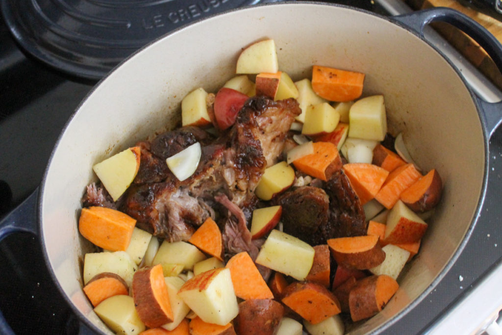 Slow cooked Dutch oven maple pork roast with the raw vegetables being added before braising in the oven.