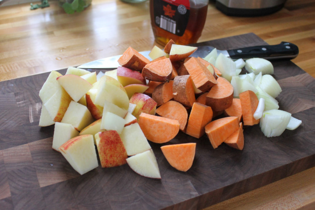 One Pot Maple Pork Roast Ingredients chopped on a cutting board including sweet potato, onion and apple.