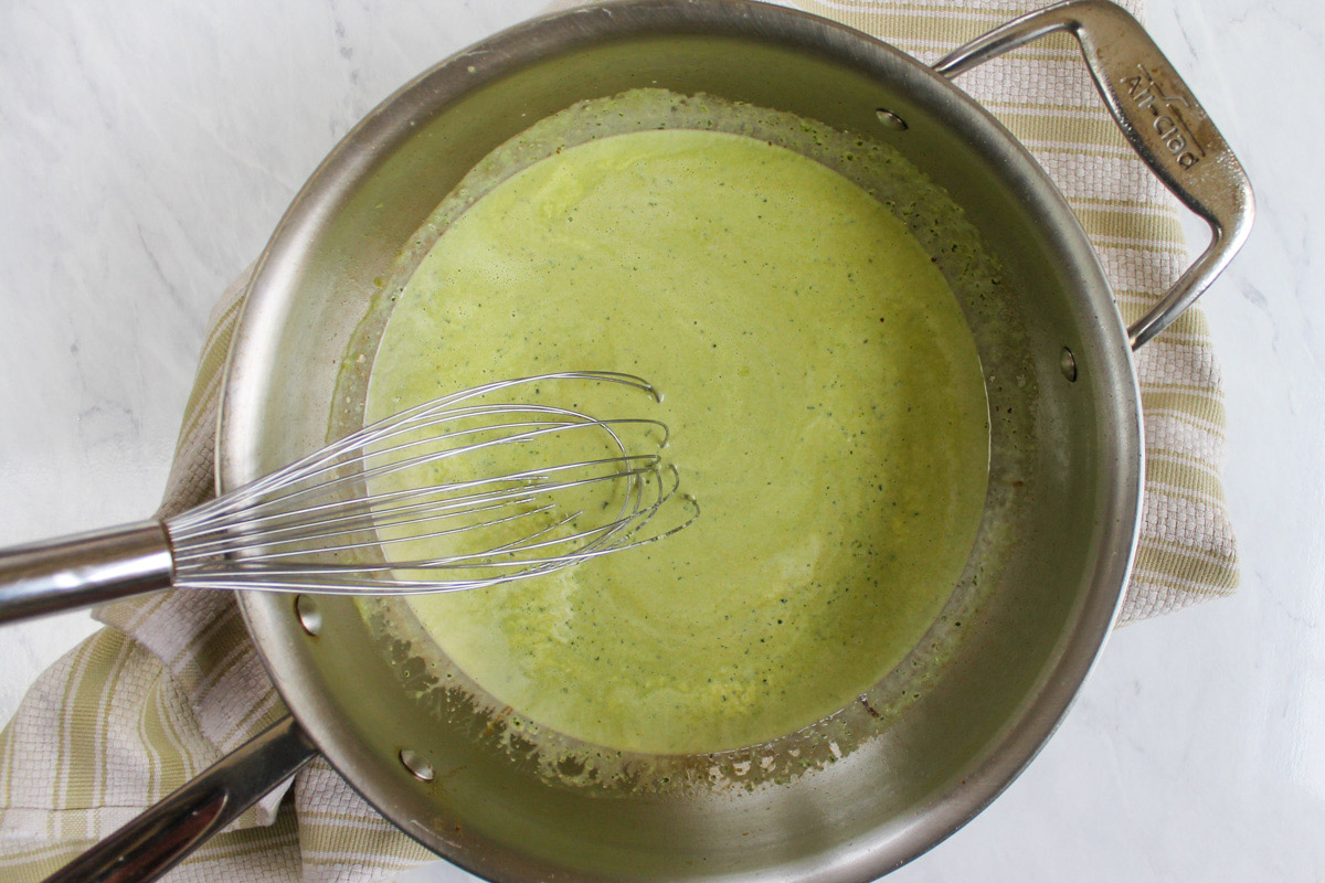 Pesto Alfredo Sauce in a skillet with a whisk.