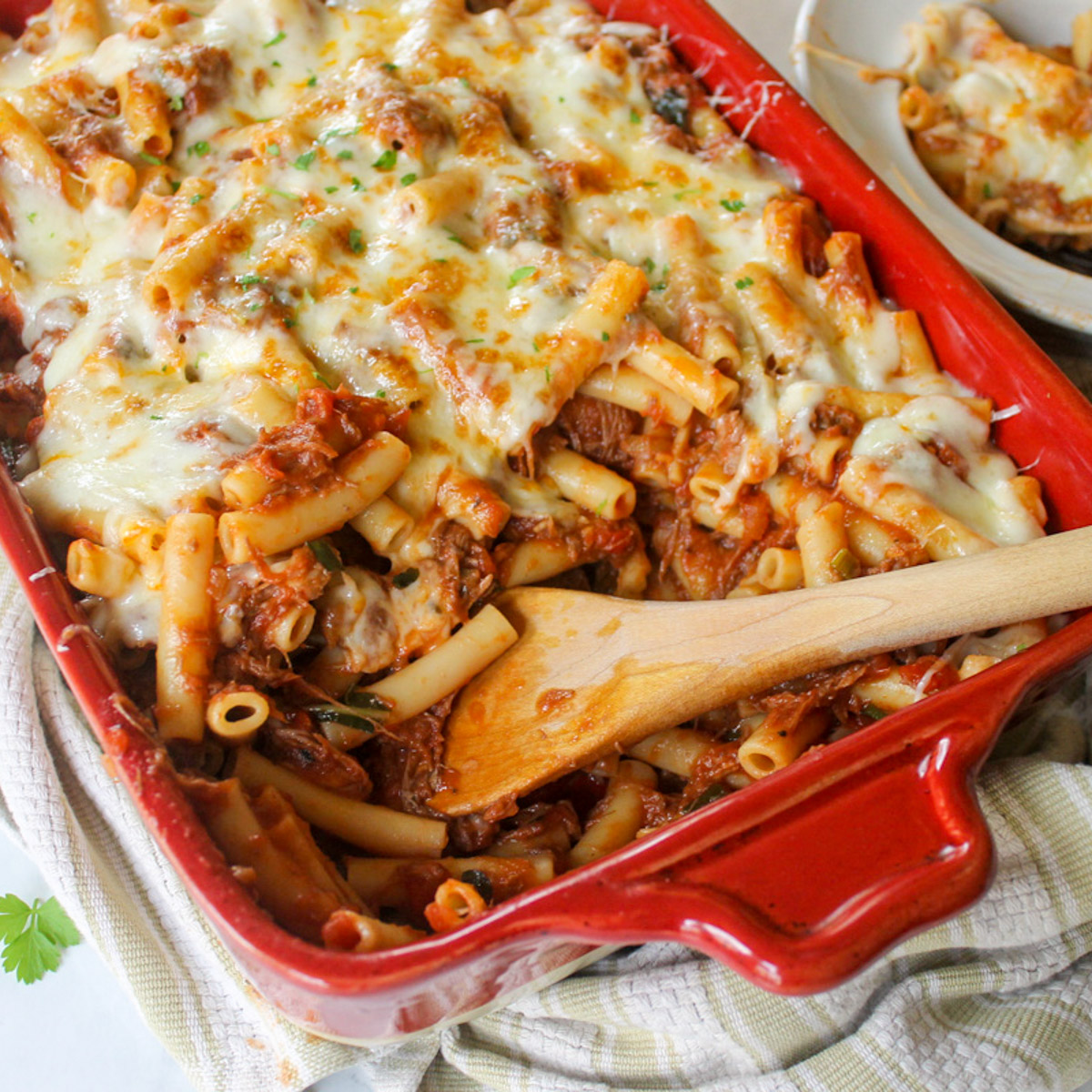 A wooden spoon serving ragu pasta bake with ziti noodles in a beef marinara sauce.