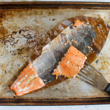 A spatula serving a piece of salmon from a sheet pan where the skin is left on the pan.