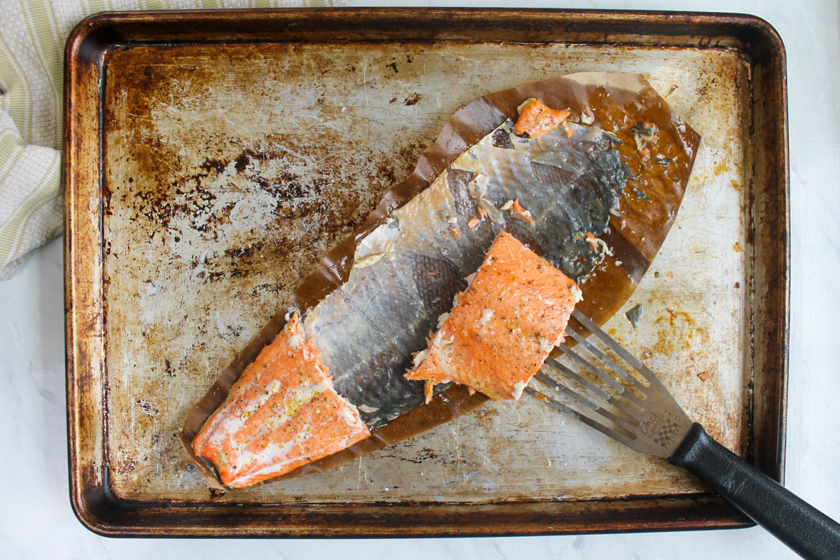 A spatula serving a piece of salmon from a sheet pan where the skin is left on the pan.