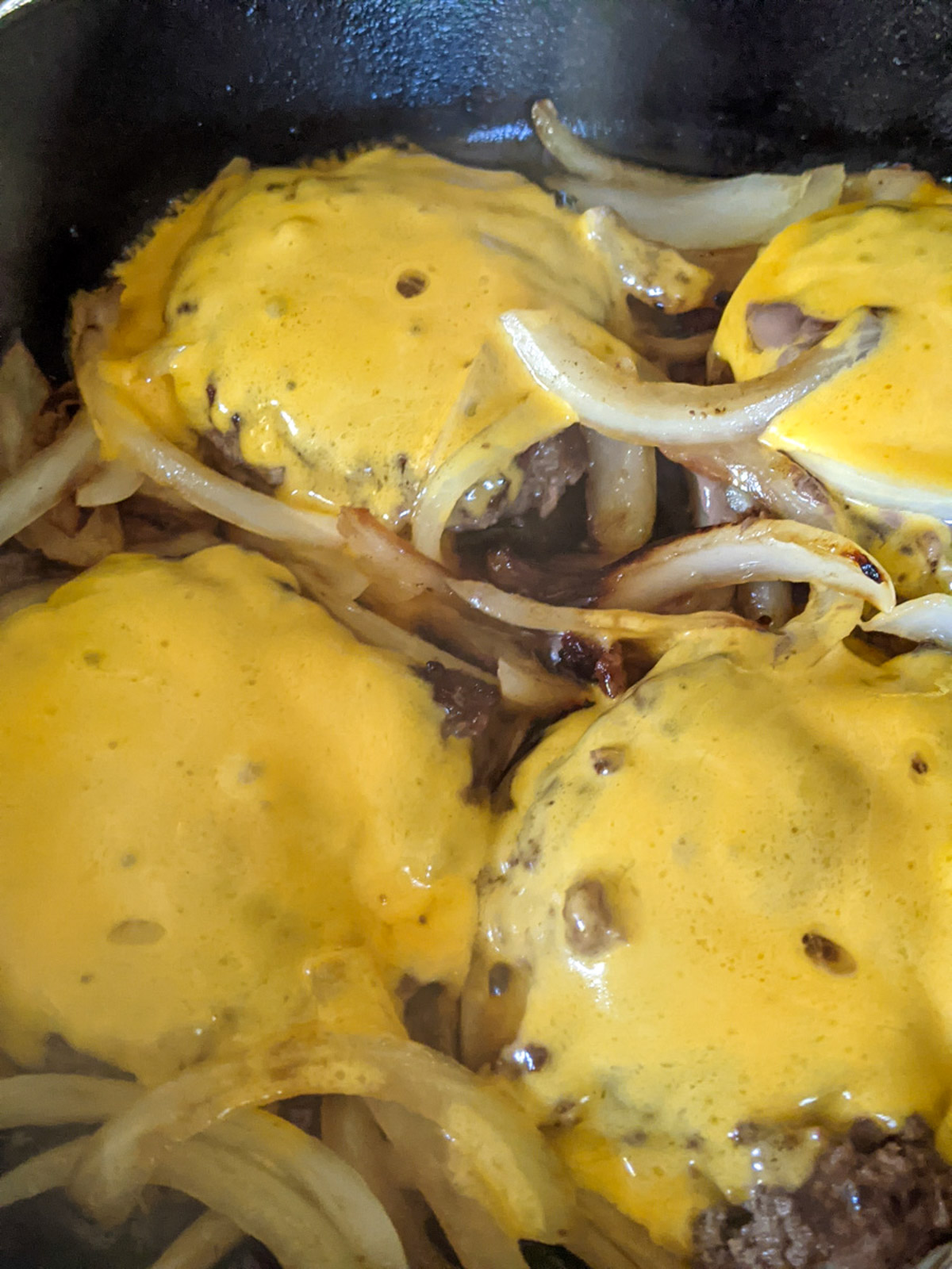 Cast iron skillet burgers covered with melted cheddar cheese and caramelized onions.