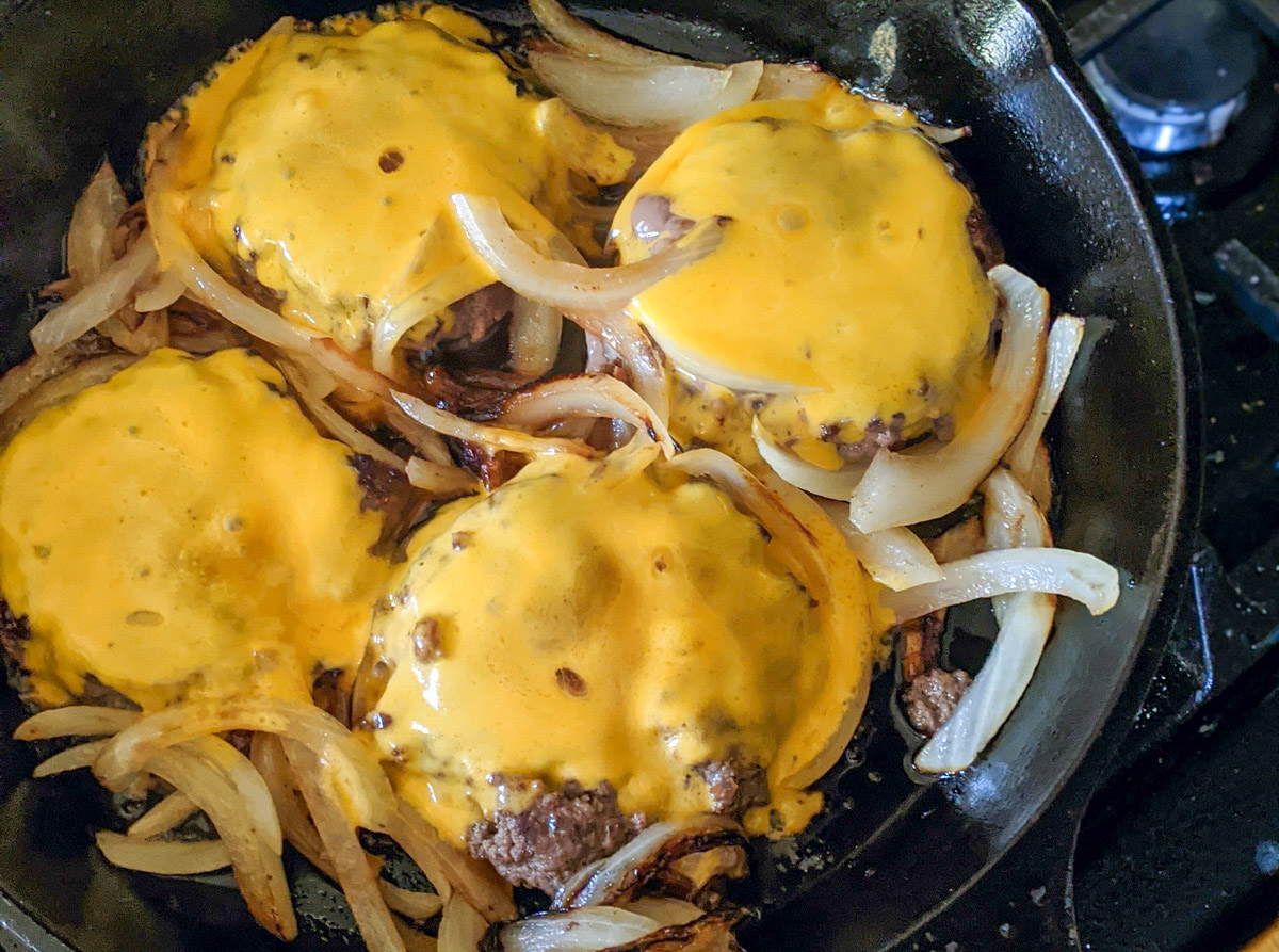 A cast iron skillet with hamburgers with melted cheese and onions.