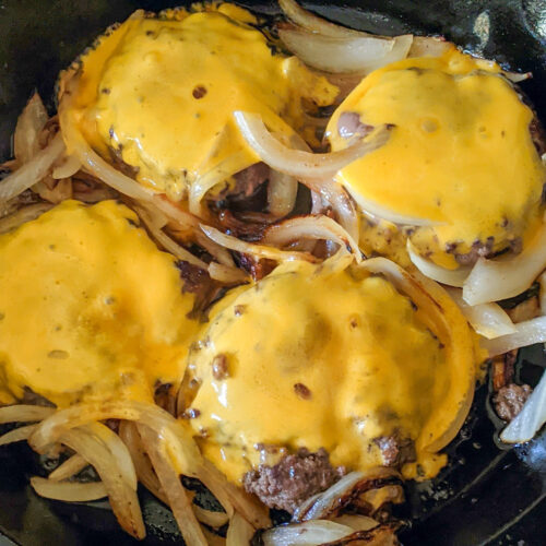 Cooking burgers in a cast iron skillet with cheese and onions.