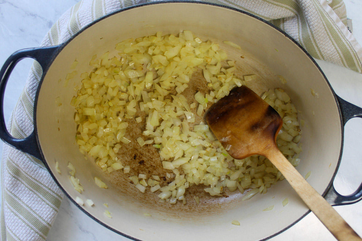 A pot of onions cooking with a wooden spoon.