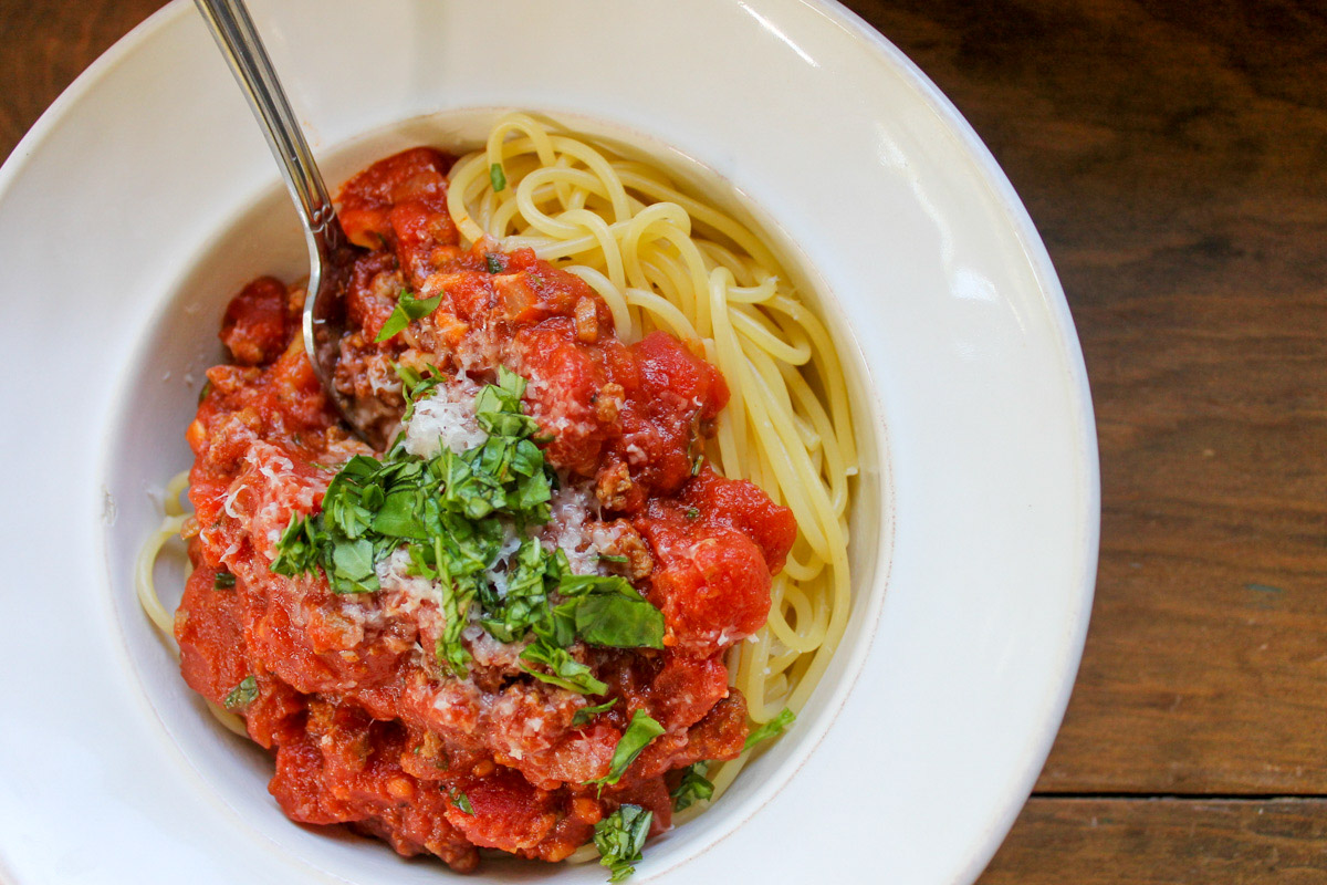 A white bowl of spaghetti and meat sauce with Parmesan cheese and basil.