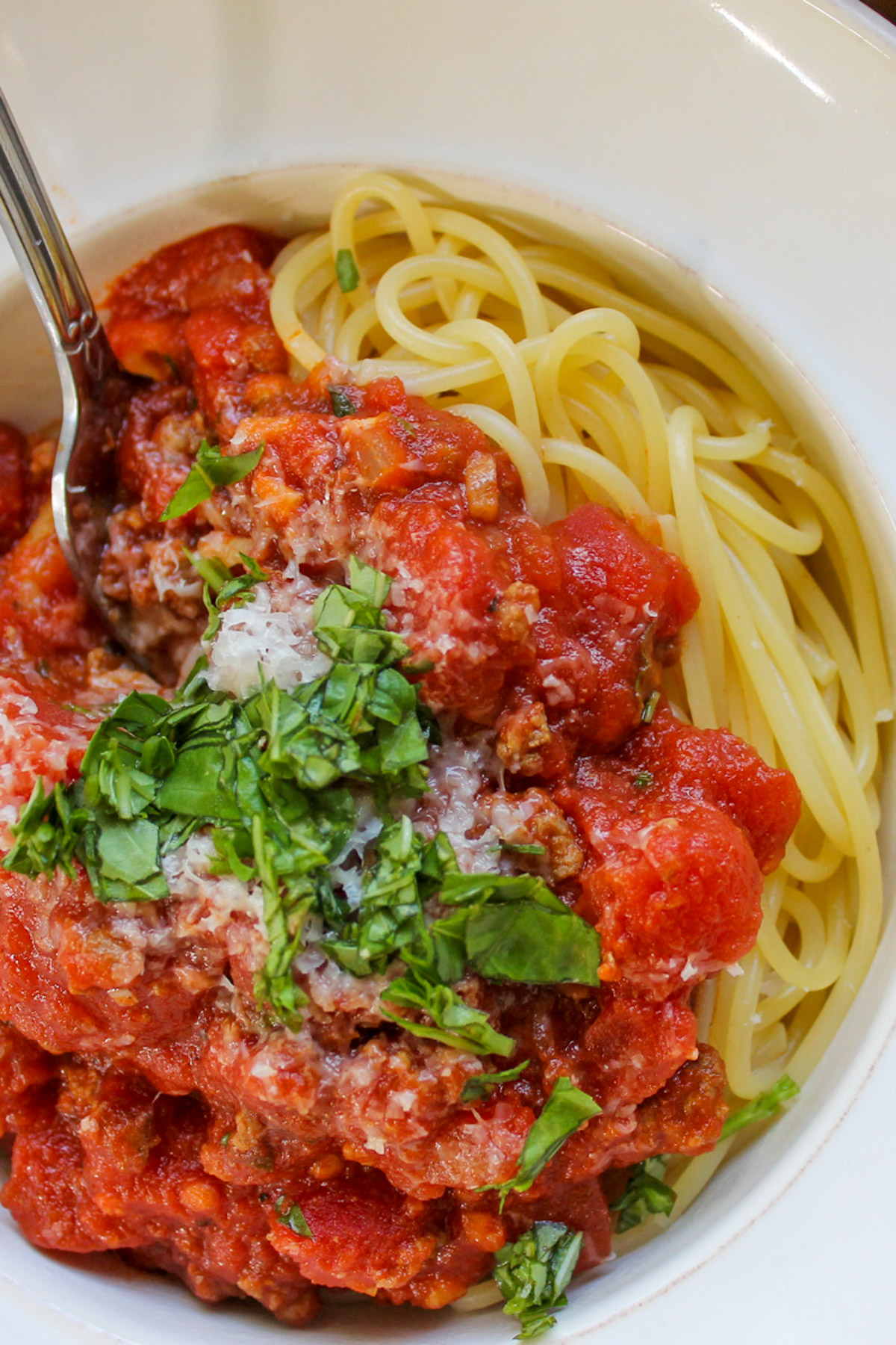 A close up of spaghetti meat sauce over noodles with green fresh basil.