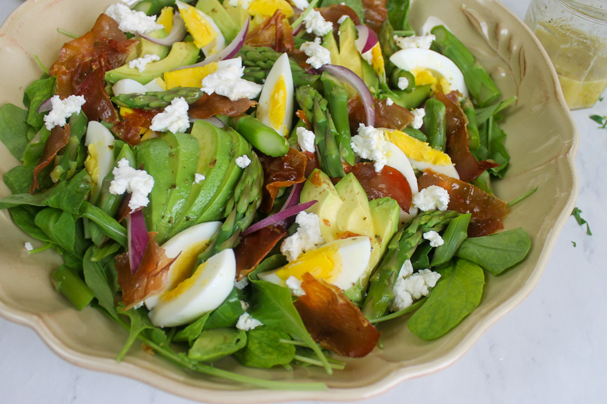 A serving dish of salad with blanched asparagus spears, hard boiled eggs, and crispy prosciutto.