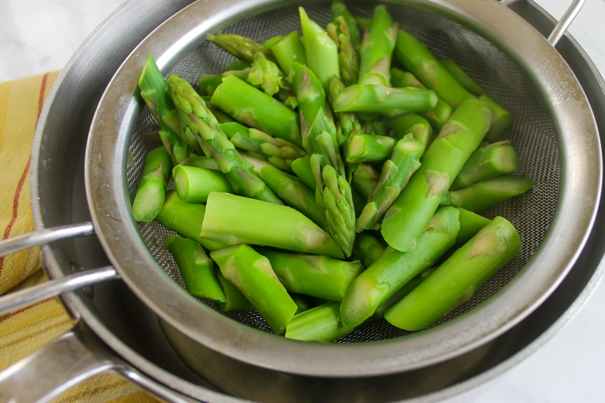 Sliced asparagus in a strainer over a pot that has been blanched.