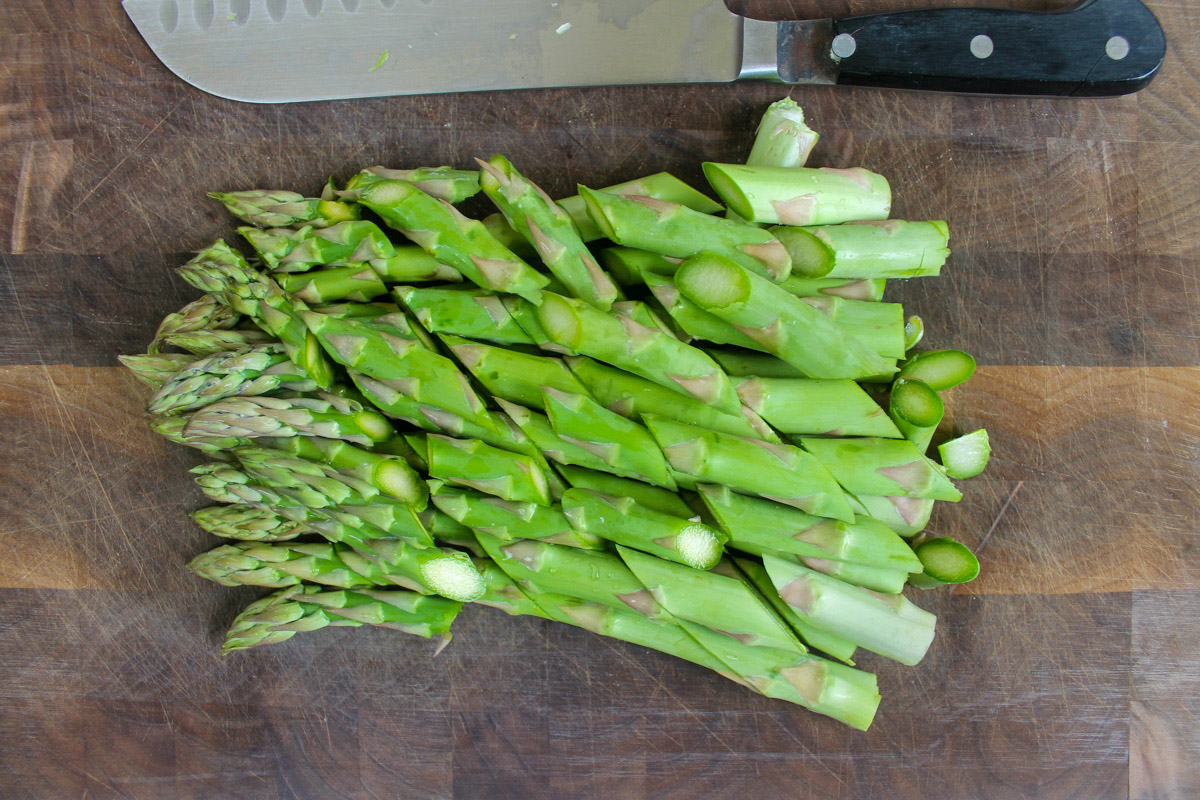 Chopped raw asparagus spears on a cutting board.