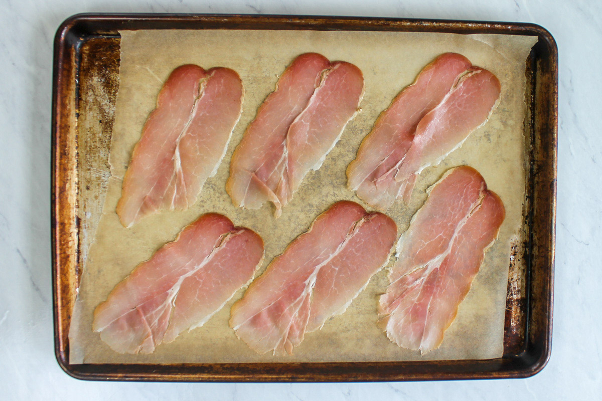 A sheet pan with slices of prosciutto ready to bake until crispy.