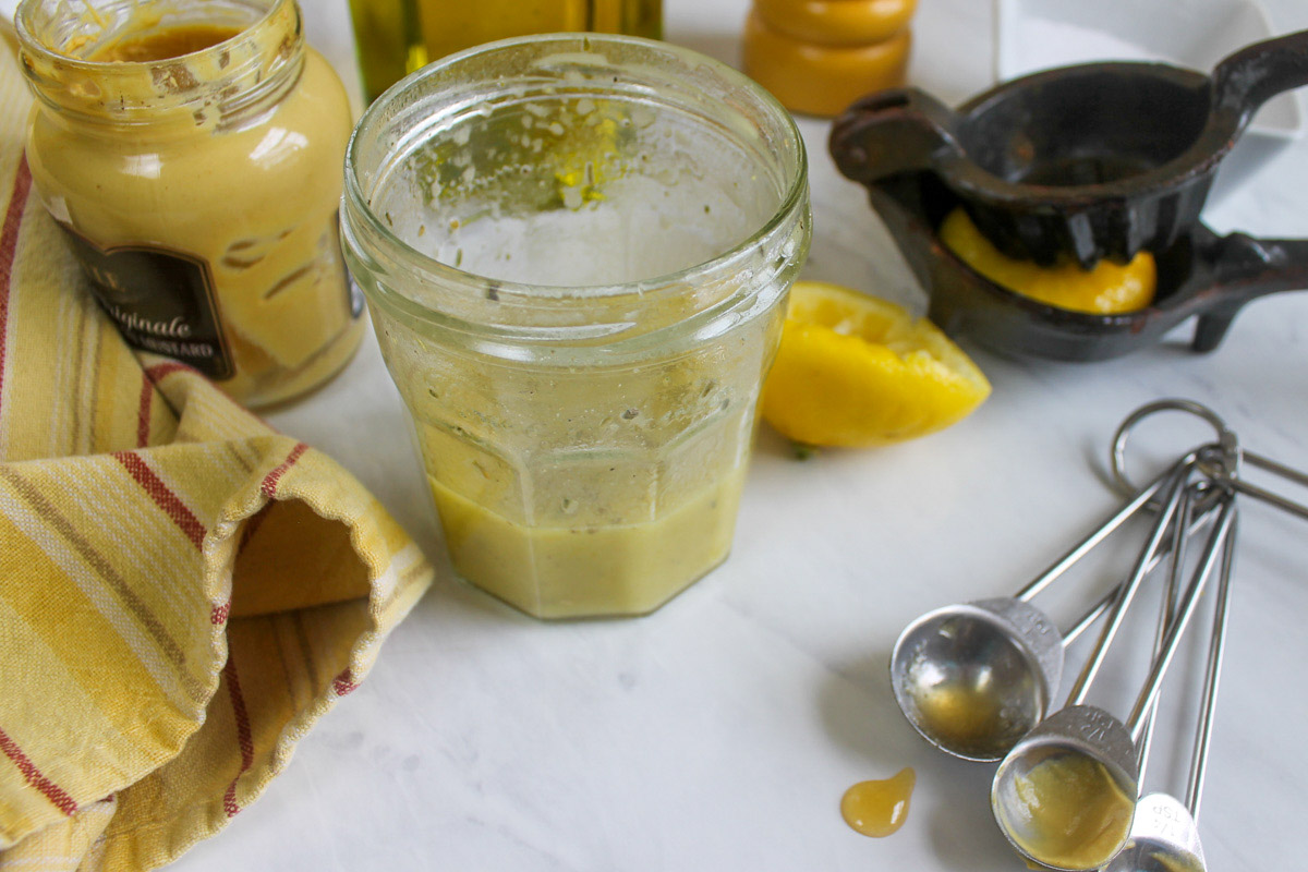 A jar of homemade vinaigrette dressing with a squeezed lemon and dijon mustard.