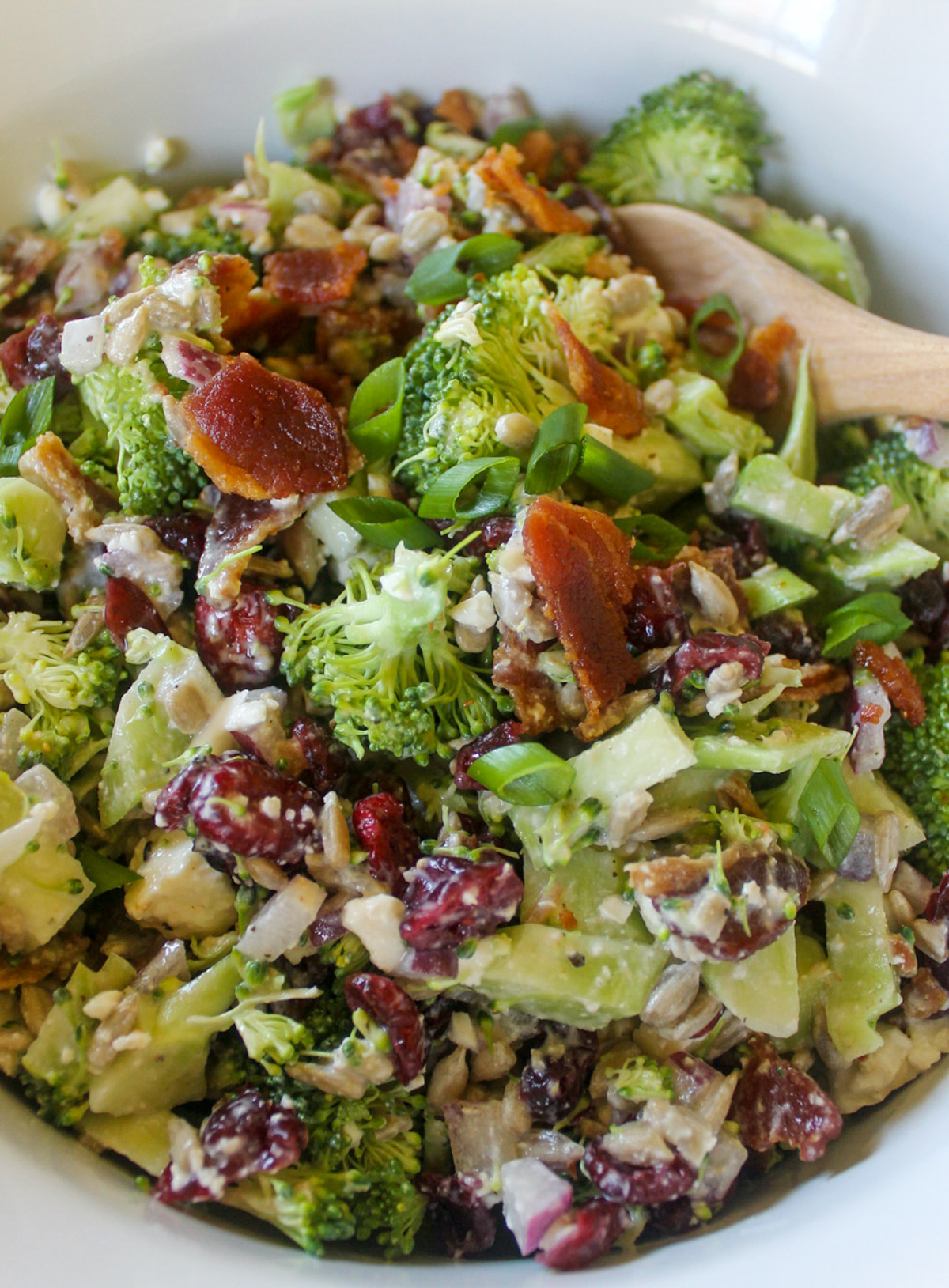 Broccoli Salad with feta, cranberries and bacon in a white dish with a wooden spoon.