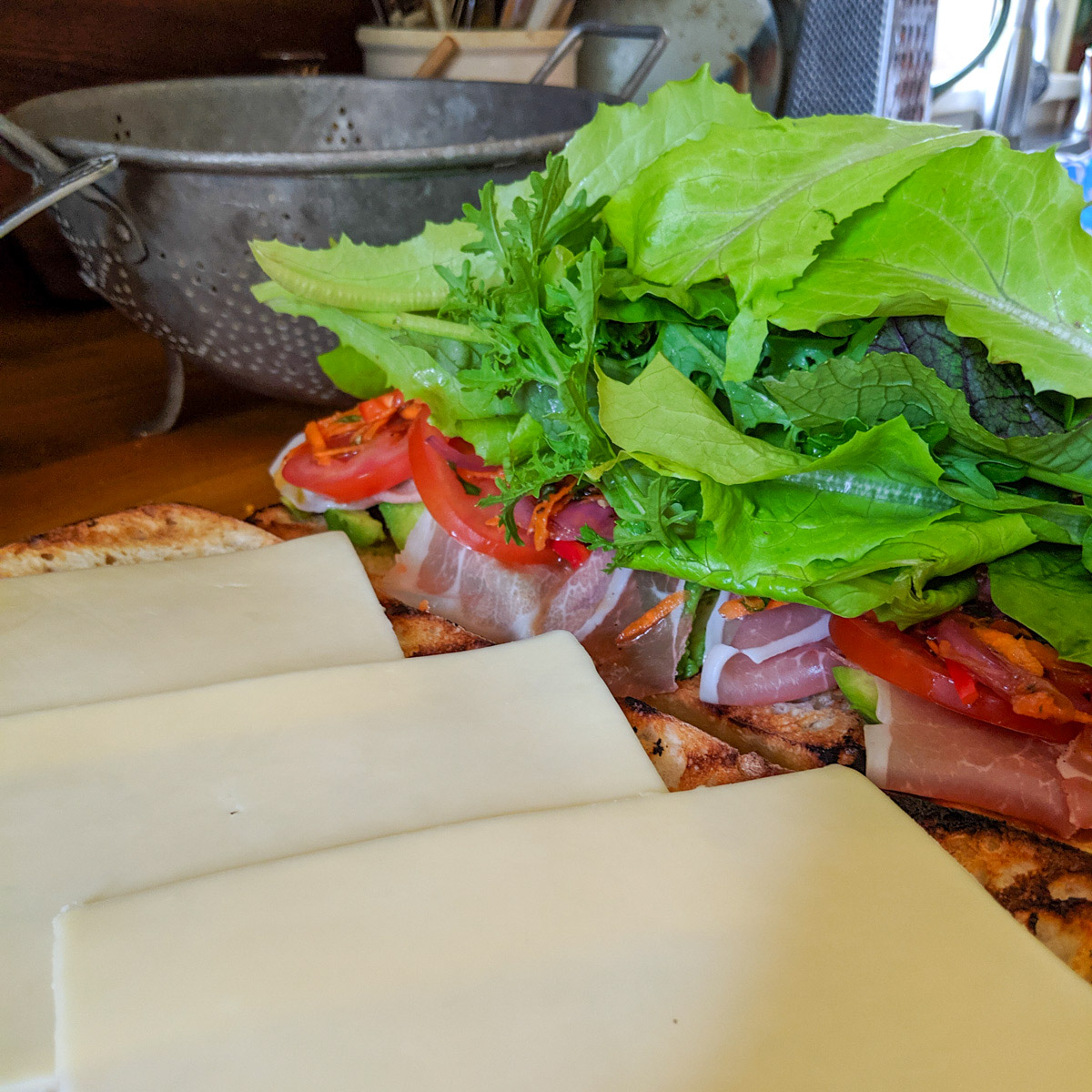 Italian Subs being made, piled with prosciutto, giardiniera and lettuce greens.