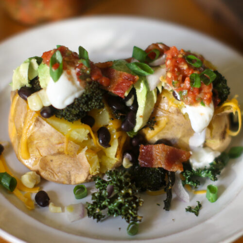 A plate of 2 loaded baked potatoes with toppings.