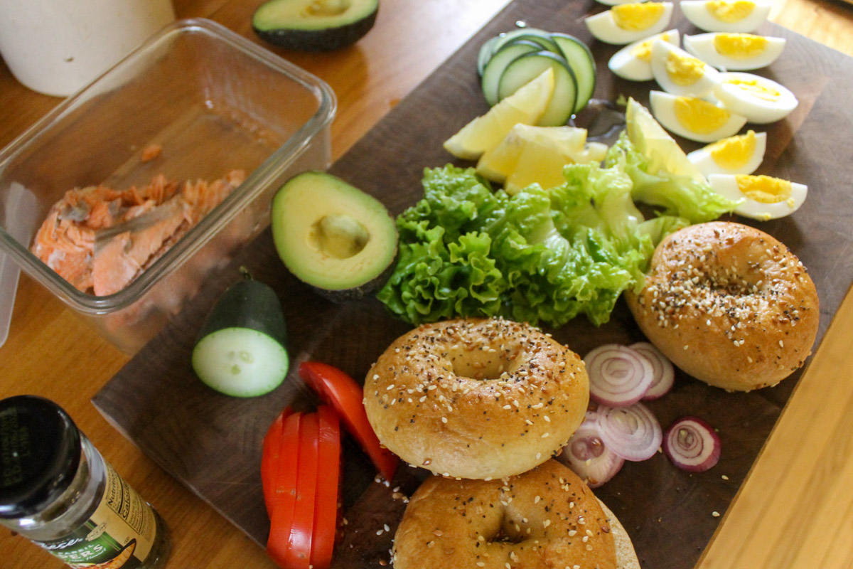 Ingredients on a cutting board for a salmon avocado bagel platter.