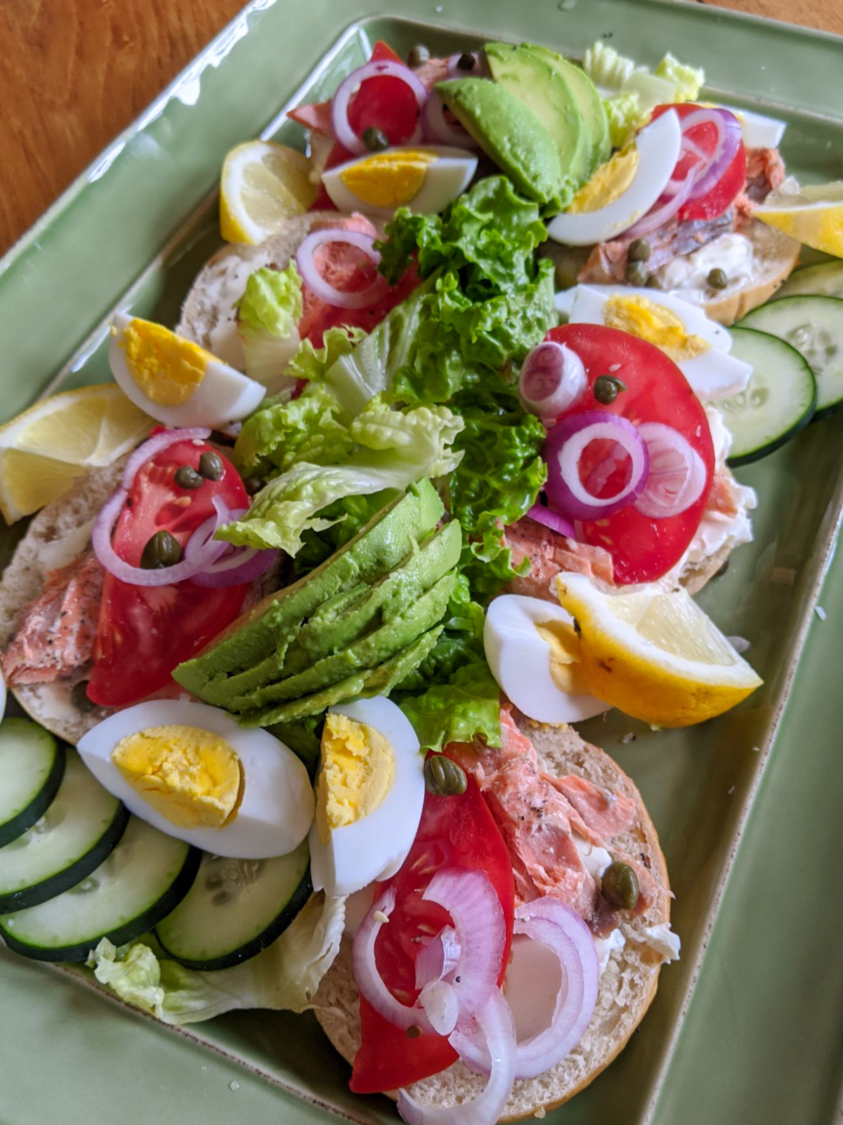 Avocado Salmon Bagel platter with tomato, red onion, capers, lemon and cucumber.