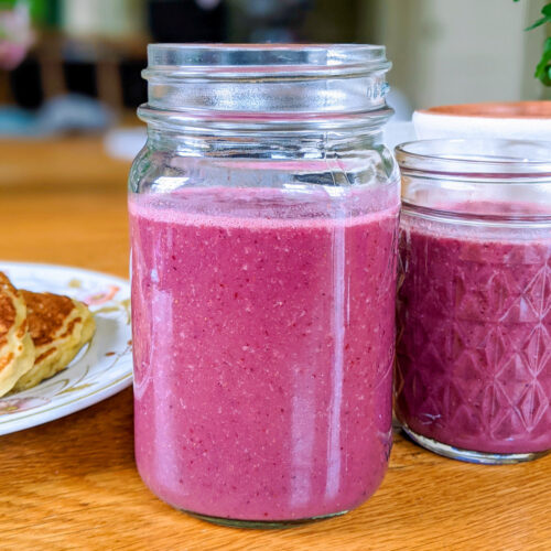 Jar of pink fruit smoothies on a table.