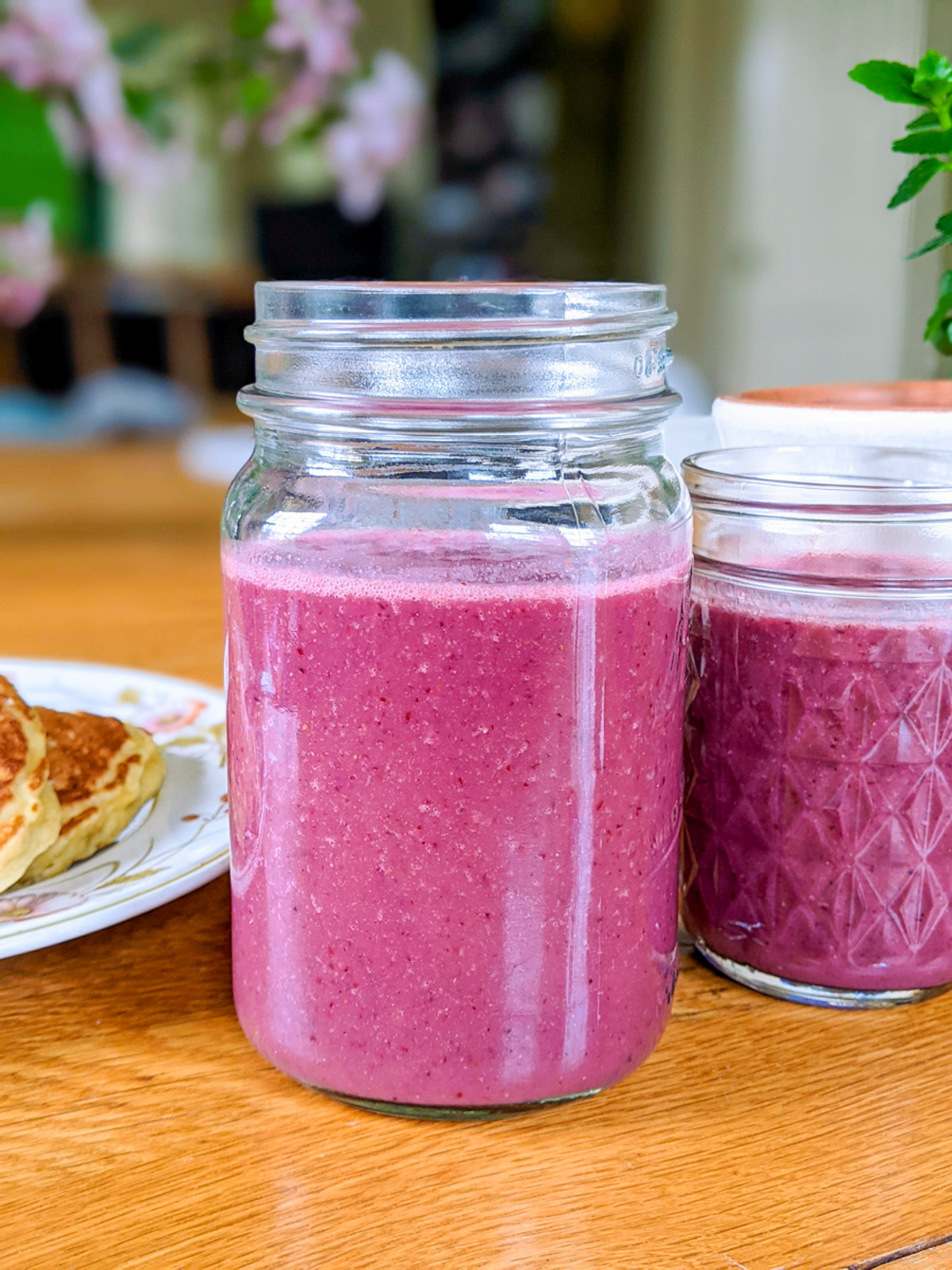 Two mason jars of bright pink smoothies made with fruit on a table.